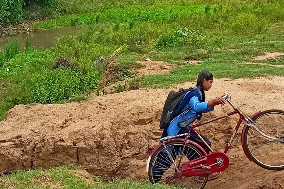 साइकिल लेकर नदी पार करती छात्रा.