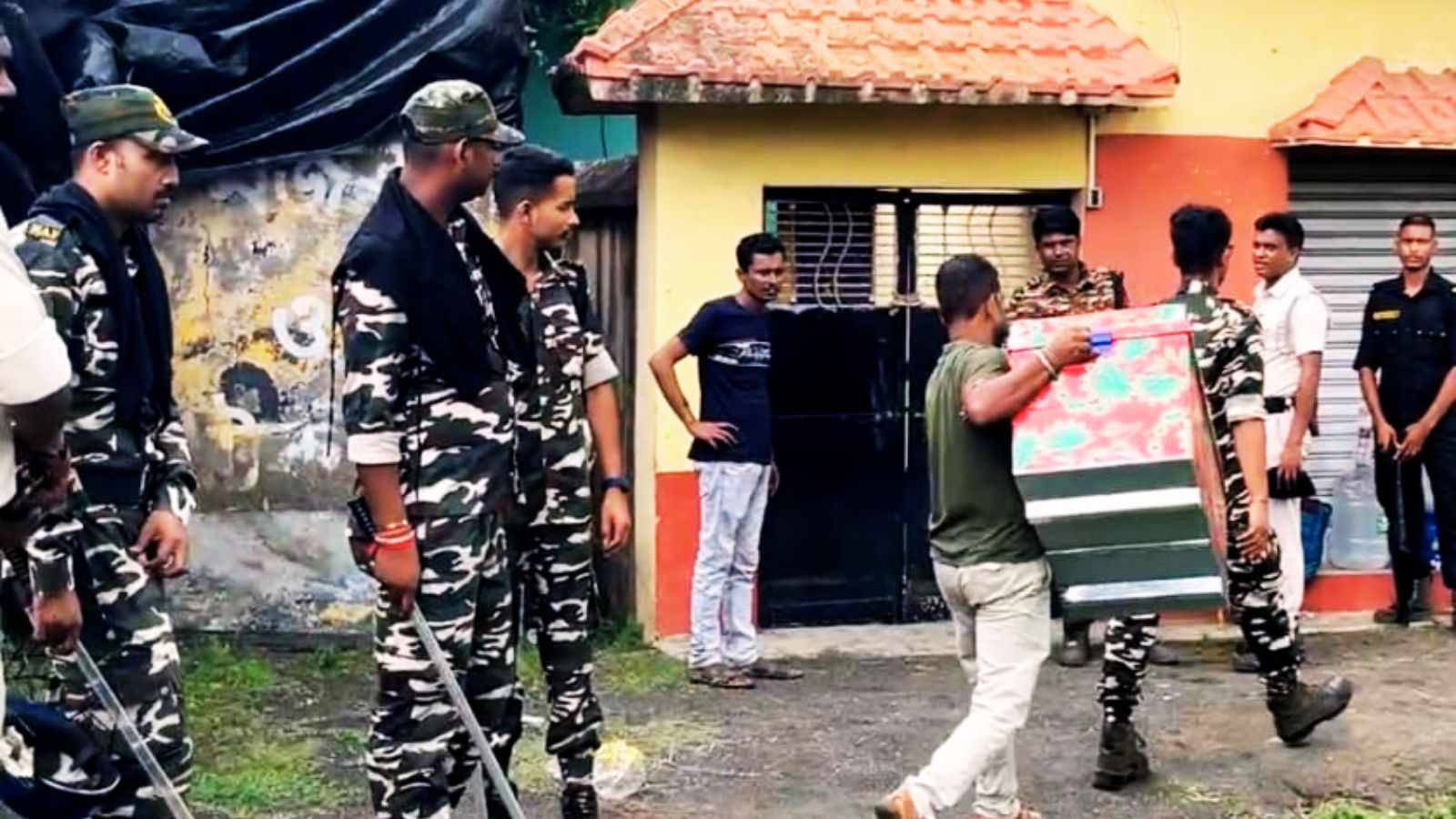 मोनिर के घर के बाहर सुरक्षा में तैनात जवान और जब्त की गयी चीजें ले जाने के लिए मंगायी गयी बड़ी पेटी.