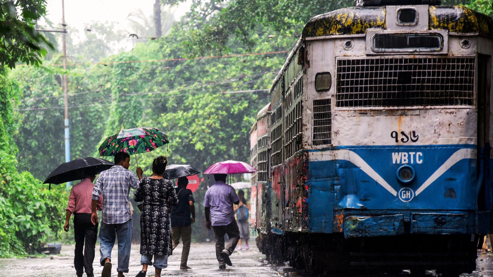 कोलकाता में भारी बारिश और भीगने से बचने के लिए छाते लेकर चलते लोग.