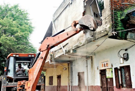 जेसीबी से मकान को तोड़ता कर्मचारी