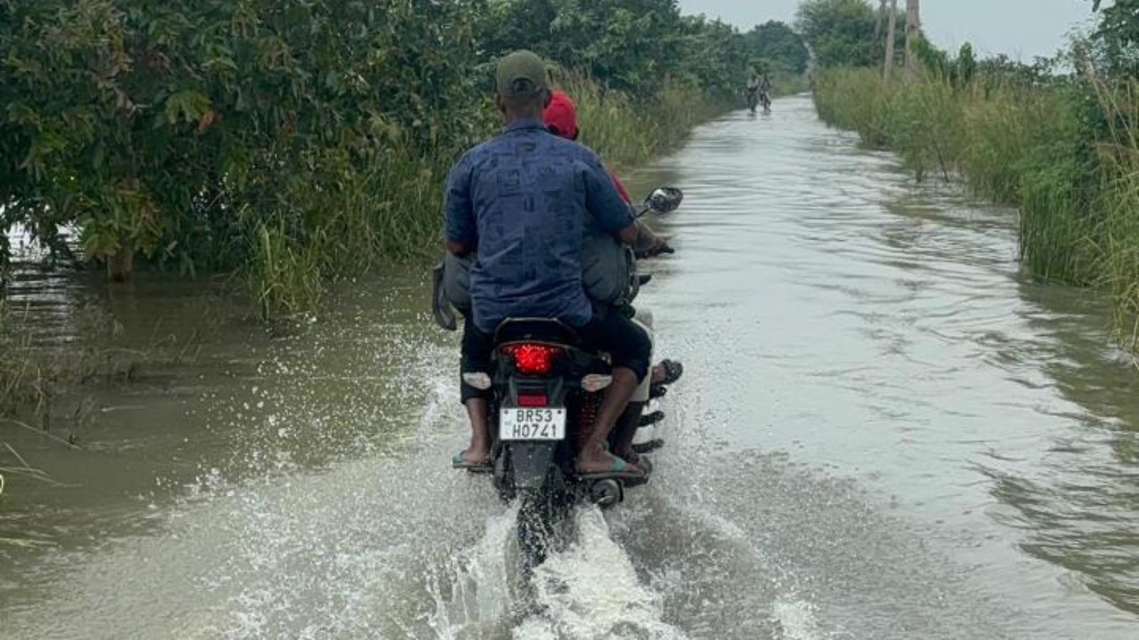 बाढ़ के पानी से गुजरते मोटर साइकिल चालक